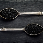 Two vintage silver spoons with black sturgeon caviar on black slate stone background. Top view, flat lay, copy space